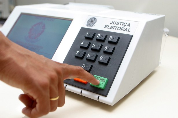 Mão masculina confirmando voto na urna eletrônica.