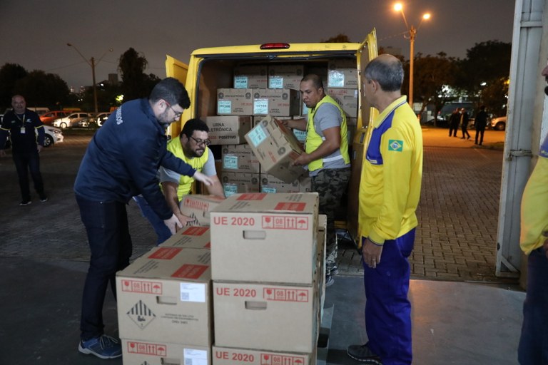 Fotografia de caixas de urnas eletrônicas sendo acomodadas em um veículo por funcionários dos Co...