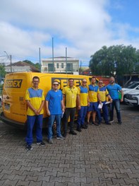 Fotografia em ambiente externo na qual se observam cinco pessoas de peles claras posando sorride...