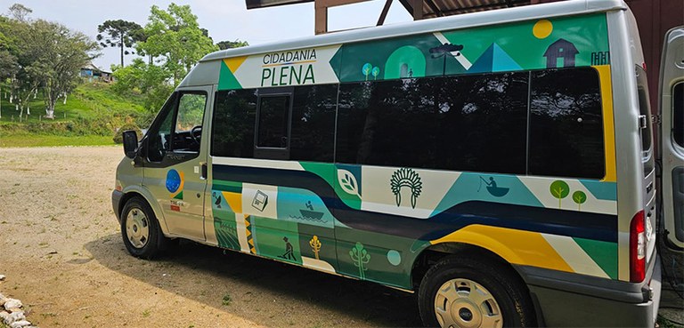 Van, com figuras de árvores, pessoas, casas e urna eletrônica coloridas em verde, azul, amarelo ...