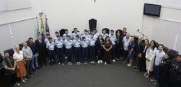 Fotografia na qual é possível ver estudantes e autoridades posando sorrindo, no plenário da Câma...