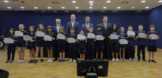 Fotografia em que se observa um grupo de quinze crianças, entre meninos e meninas, e quatro home...