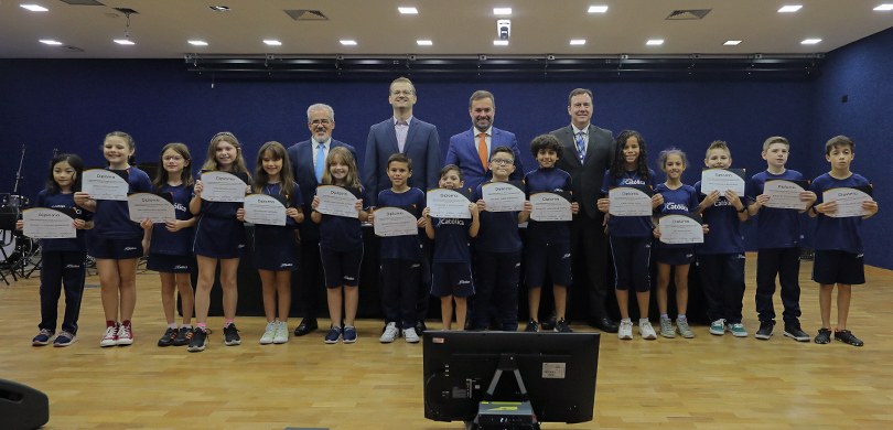 Vereadores mirins do Colégio Católica de Curitiba são diplomados Fotografia em que se observa um grupo de quinze crianças, entre meninos e meninas, e quatro home...
