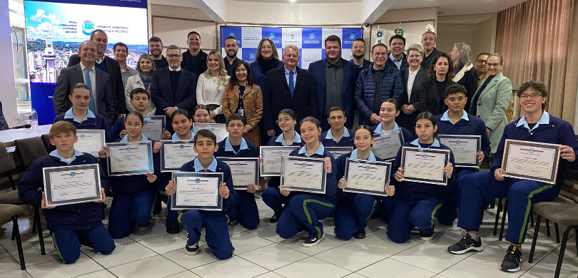 Vereadores mirins tomam posse na Câmara Municipal de Francisco Beltrão Fotografia de diversas pessoas, entre homens e mulheres, posando sorrindo em um sala com paredes...