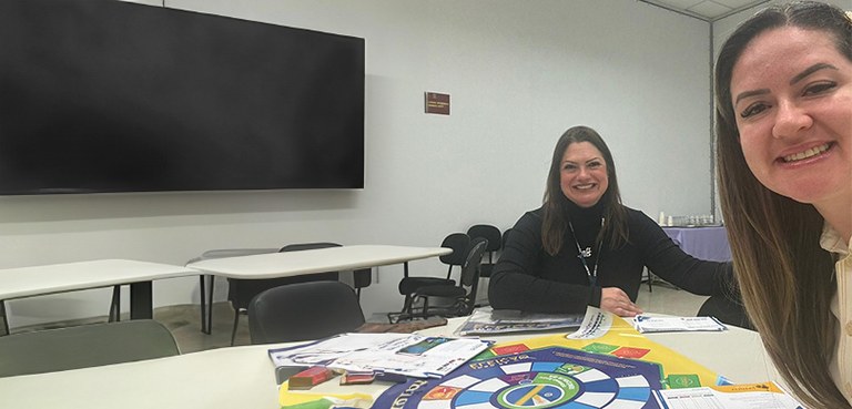Vereadores mirins visitam a sede do TRE-PR 3 Fotografia, em estilo selfie, de duas mulheres sorrindo, sentadas ao redor de uma mesa branca, o...