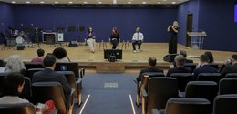 Fotografia de um auditório onde ocorre uma palestra ou debate. Em primeiro plano, vê-se a platei...