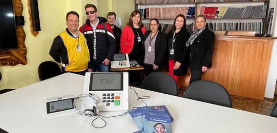 Fotografia de um grupo de pessoas em uma sala com paredes azuis. Algumas pessoas utilizam cadeir...