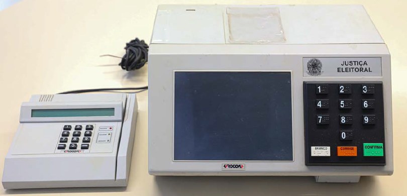 Fotografia de uma urna eletrônica sobre uma mesa branca.