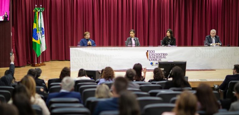 Voz da urna eletrônica, cantora Sara Bentes grava clipe no TRE-PR para incentivar mesários com deficiência 2 Fotografia de um palco de auditório em que há duas mulheres e dois homens sentados atrás de uma ...