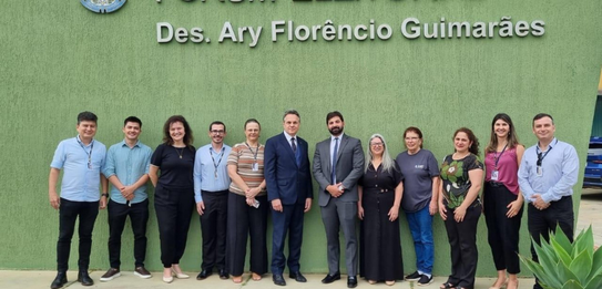 Fotografia na qual é possível ver dez mulheres e cinco homens posando sorrindo. Ao fundo, está a...