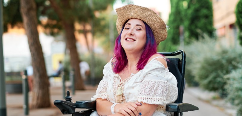 Em um ambiente rodeado por árvores, vê-se uma mulher com o cabelo pintado de rosa e azul sentada...
