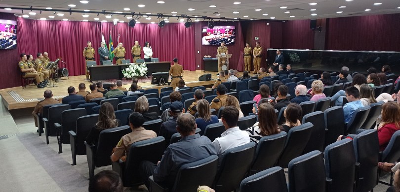 Fotografia de um auditório em que se vê, em primeiro plano, homens e mulheres sentados em cadeir...