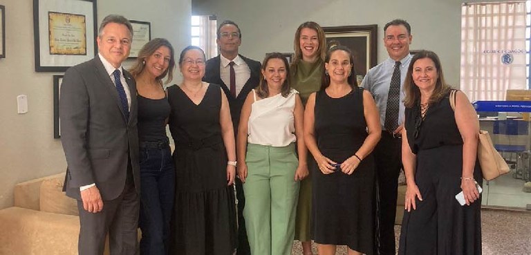 Em uma sala com paredes brancas e quadros pendurados na parede, três homens e seis mulheres, usa...