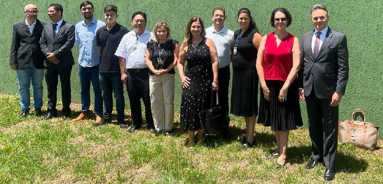 Fotografia de homens e mulheres em pé sobre um gramado, em frente a uma parede verde.