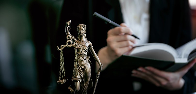 Dia do Advogado: conheça histórias de profissionais da área eleitoral Fotografia de uma estatueta da dama da Justiça em bronze. Ao fundo, desfocado, observa-se uma mu...