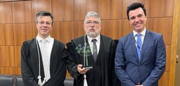 Fotografia de três homens, dois deles vestindo togas pretas e um deles vestindo paletó e gravata...