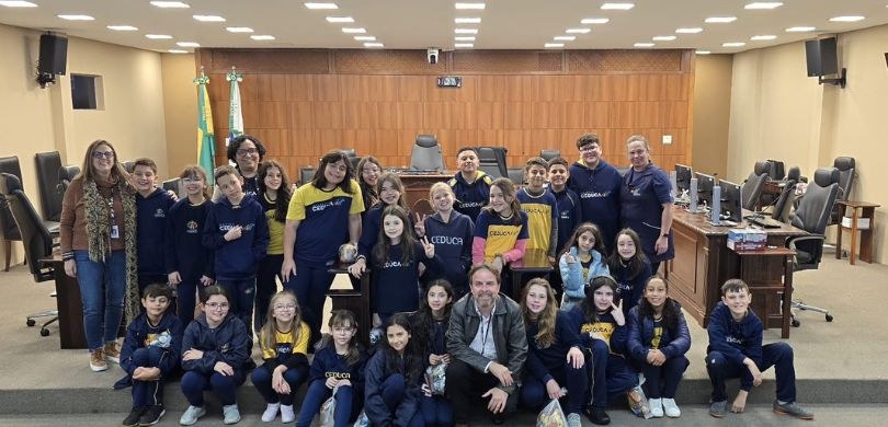 A fotografia mostra alunas e alunos posando sorrindo um ao lado do outro. Eles vestem moletons n...