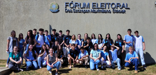 Fotografia que retrata um grupo de jovens posando para uma foto em frente à fachada do Fórum Ele...