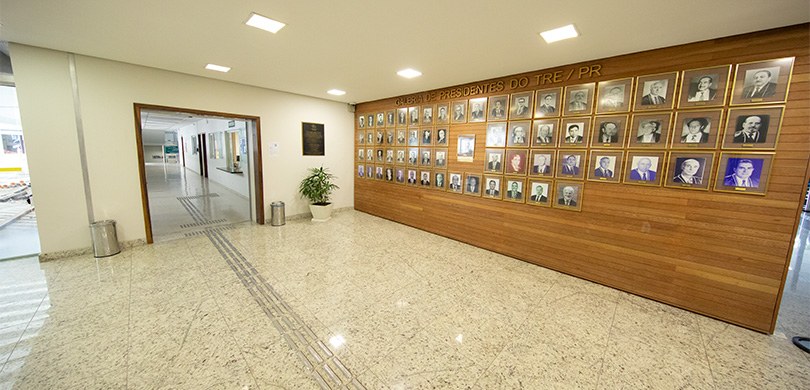 Foto de um corredor em que pode-se ver, ao lado direito, uma parede de madeira com fotografias p...