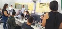 Fotografia de 4 mulheres sentadas em frente a telas de computador atendendo pessoas. Em primeiro...