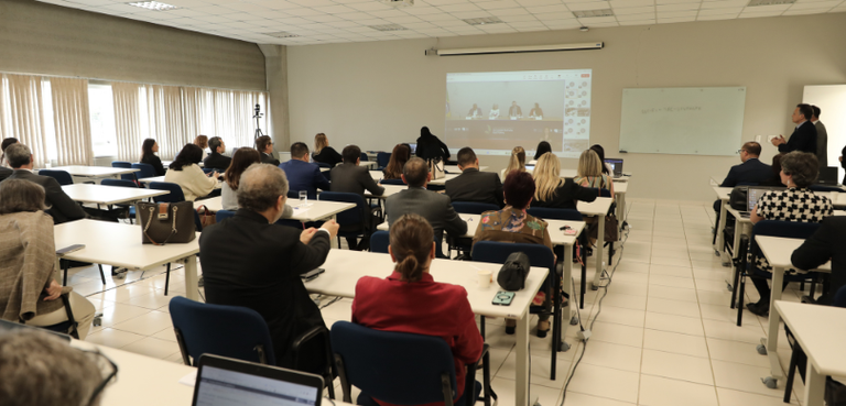 Juízes eleitorais participam do início de curso de aperfeiçoamento nesta sexta-feira (5) Fotografia na qual juízas e juízes estão sentados em duplas em mesas brancas, enquanto assistem ...