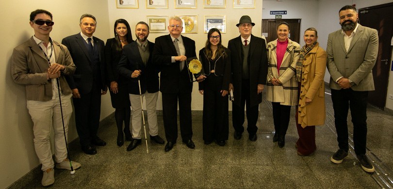 Fotografia de quatro mulheres, que vestem roupas formais de inverno, e seis homens de paletó pos...
