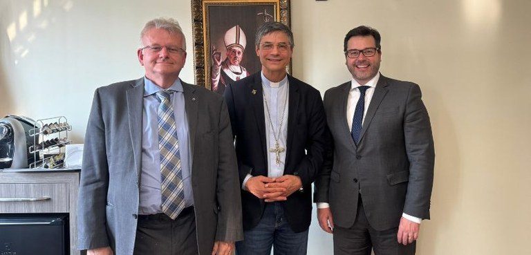 Foto em que aparecem três homens perfilados em pé. São eles o presidente Sigurd, o bispo de Casc...