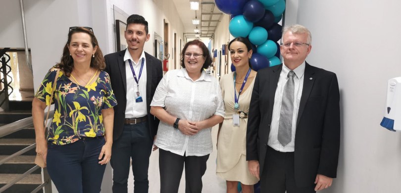 Fotografia de três mulheres, vestidas com roupas formais, e dois homens, que usam terno, posando...
