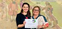 Na foto, há duas mulheres sorrindo e segurando o certificado do Prêmio Viva Inclusão 2024. A mul...