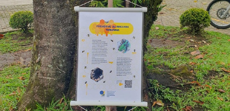 A foto mostra um banner escrito: Preserve as abelhas Tubunas. Nele também há outras informações....