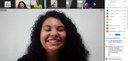 Foto da tela de uma reunião via zoom, na qual aparece em primeiro plano o rosto de uma jovem est...