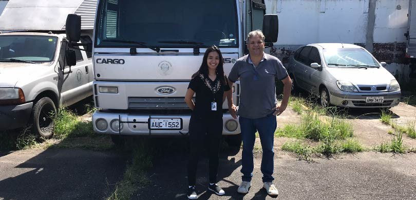 TRE-PR doa veículos a instituições Um homem e uma mulher posam em frente a um caminhão prata. Do lado esquerdo há uma caminhonete b...