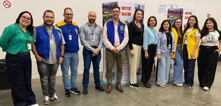 TRE-PR lança 3º Atlas Eleitoral durante 5ª edição do Paraná Faz Ciência Fotografia em que são vistas várias pessoas posando em pé em frente a cabines em que se lê “vote...