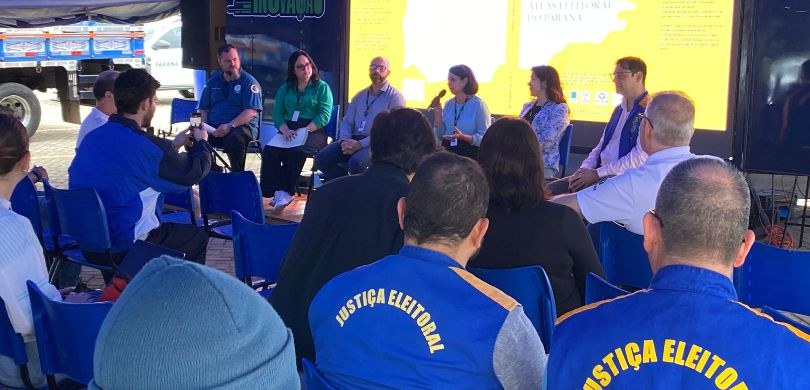 TRE-PR lança 3º Atlas Eleitoral durante 5ª edição do Paraná Faz Ciência Fotografia em que aparecem três mulheres e três homens sentados ao fundo falando para uma platei...