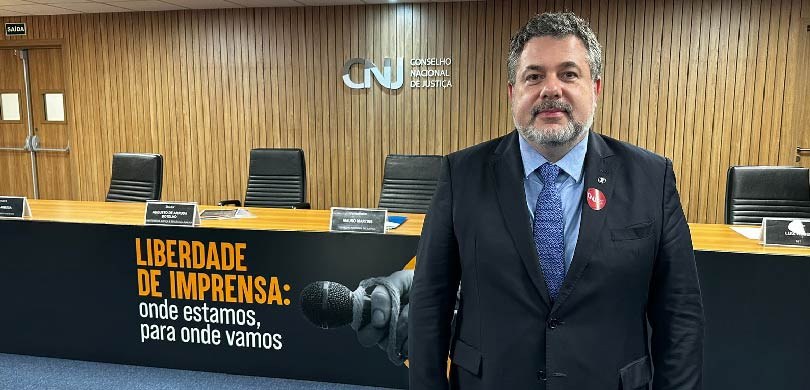 TRE-PR participa de Seminário sobre liberdade de imprensa Um homem de terno em pé, em frente à mesa do auditório do CNJ.