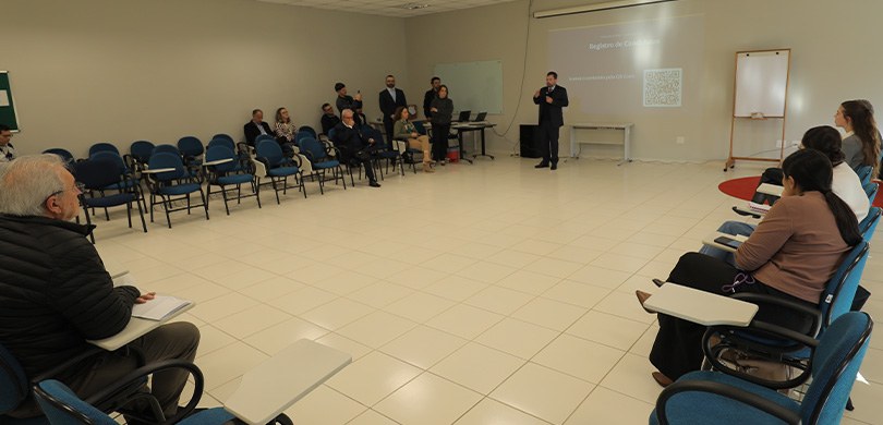 Fotografia que retrata uma reunião institucional realizada em uma sala com paredes claras e piso...