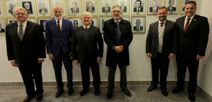 Fotografia na qual se observa um grupo de seis homens, lado a lado, posando sorrindo para a câme...