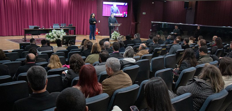 No auditório do TRE-PR, o presidente Coimbra de Moura está em cima do palco, ao lado de uma inté...